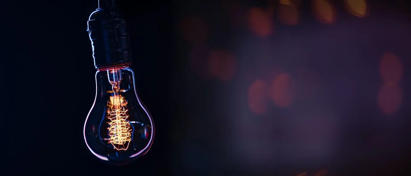 Eine leuchtende Lampe hängt im Dunkeln vor unscharfem Hintergrund, mit Platz für Text.